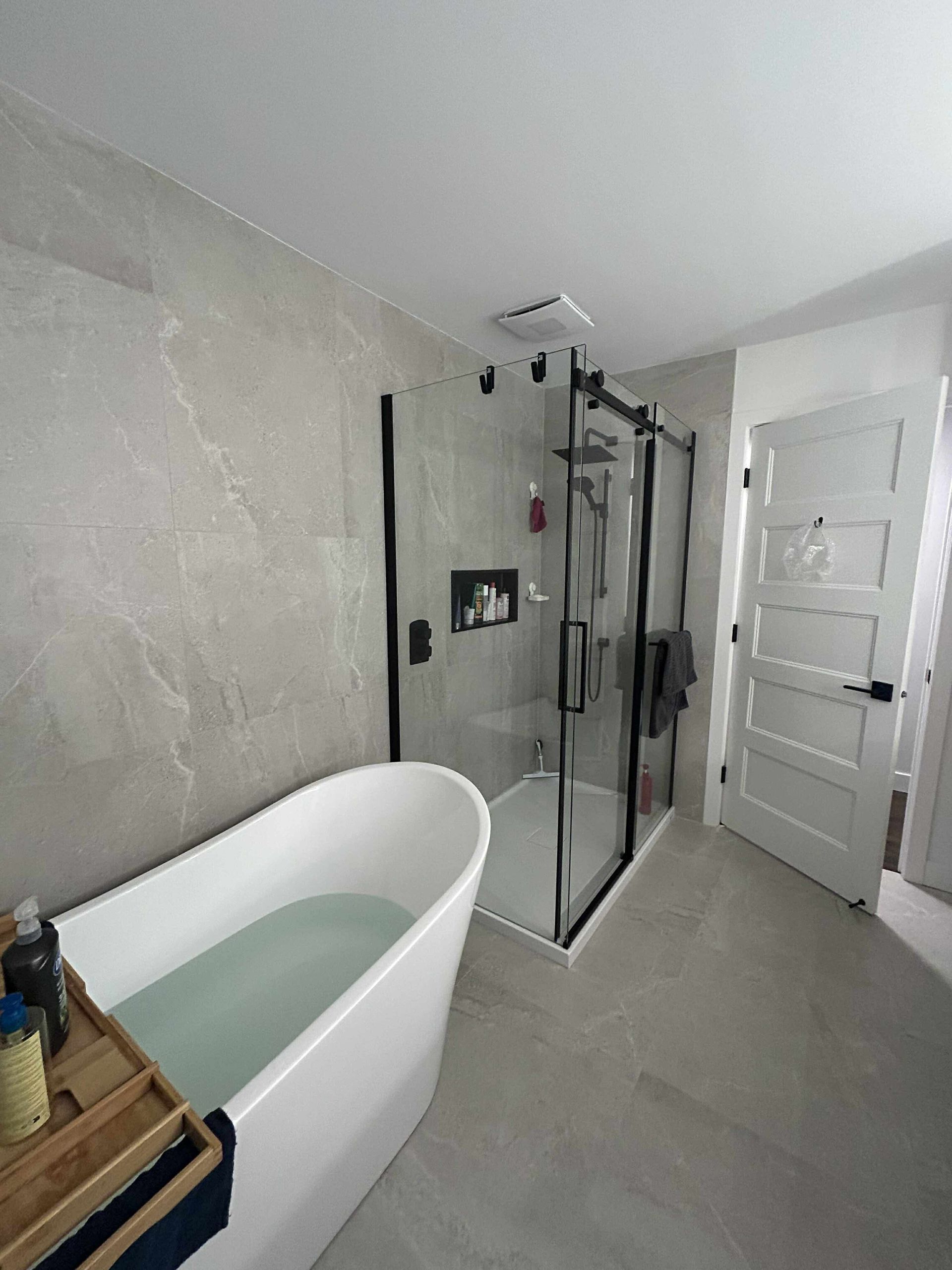 Une salle de bains moderne comprenant une baignoire îlot blanche, une douche vitrée et une porte à panneaux blancs.