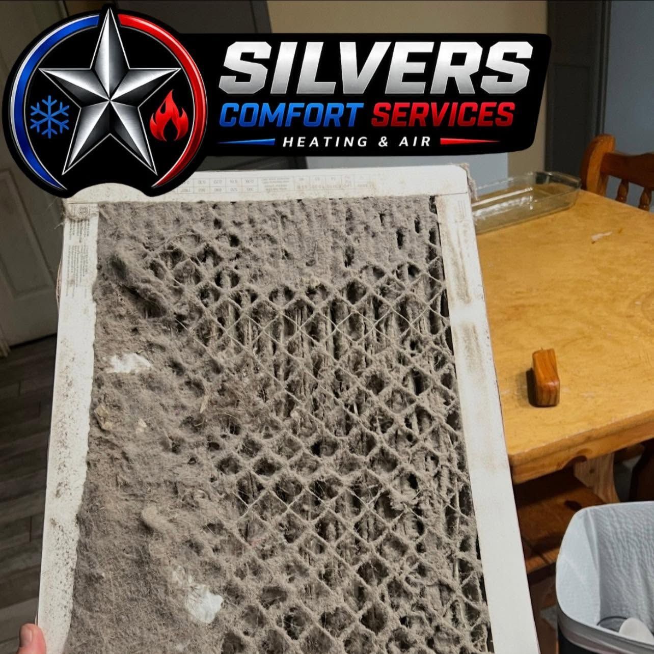 Dirty HVAC air filter on a table with a Silvers Comfort Services logo above it