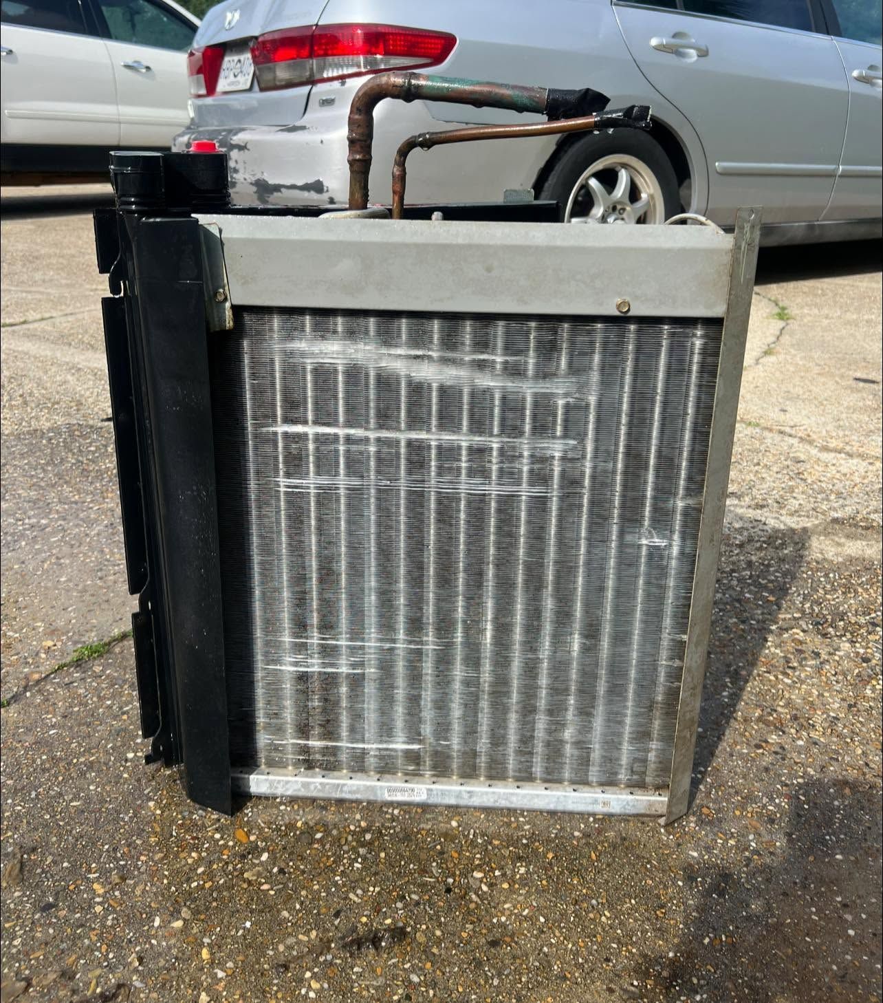 Old car radiator or condenser standing on pavement in front of a parked silver SUV