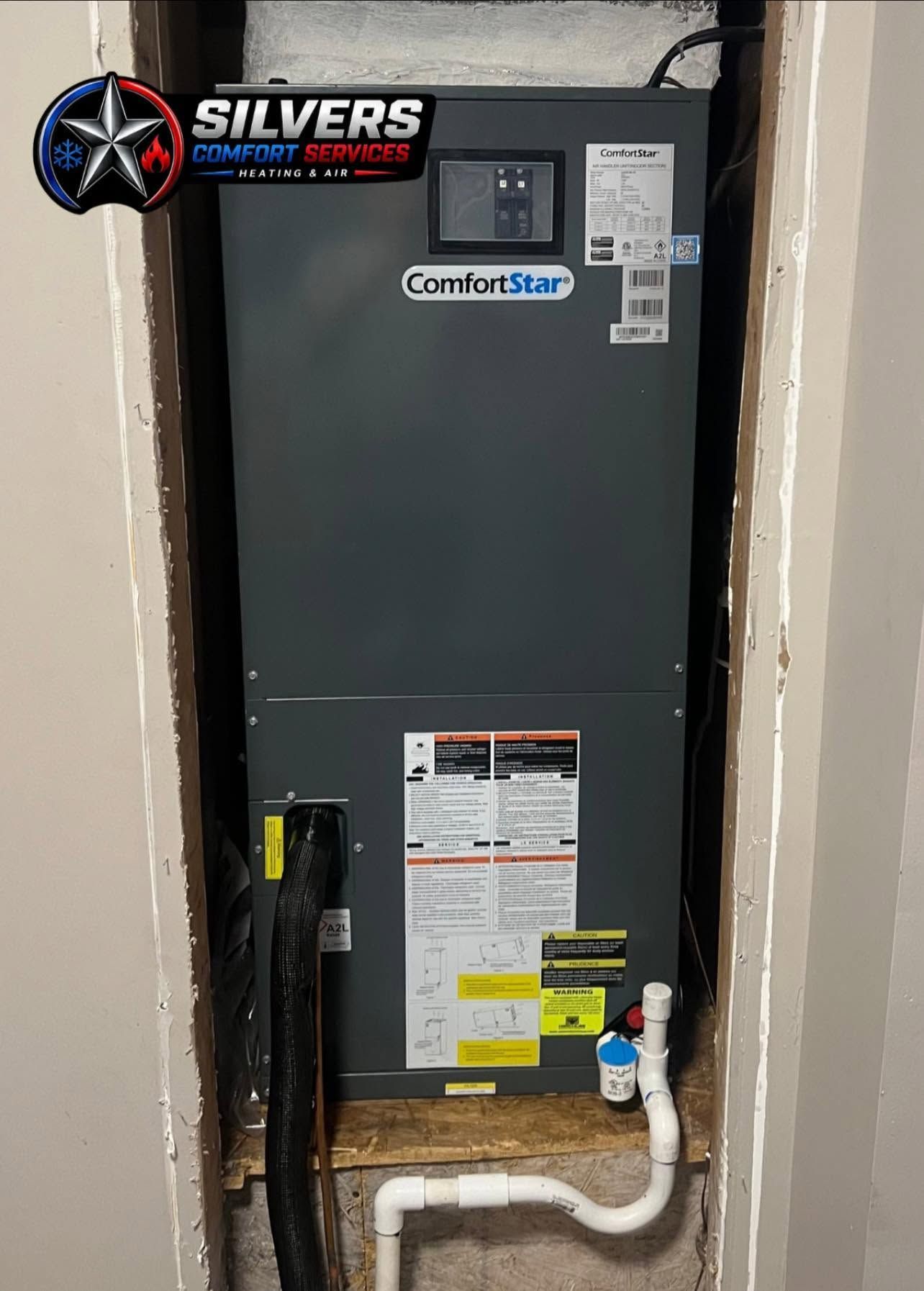 Gray furnace in a utility closet with a white pipe and yellow warning labels.