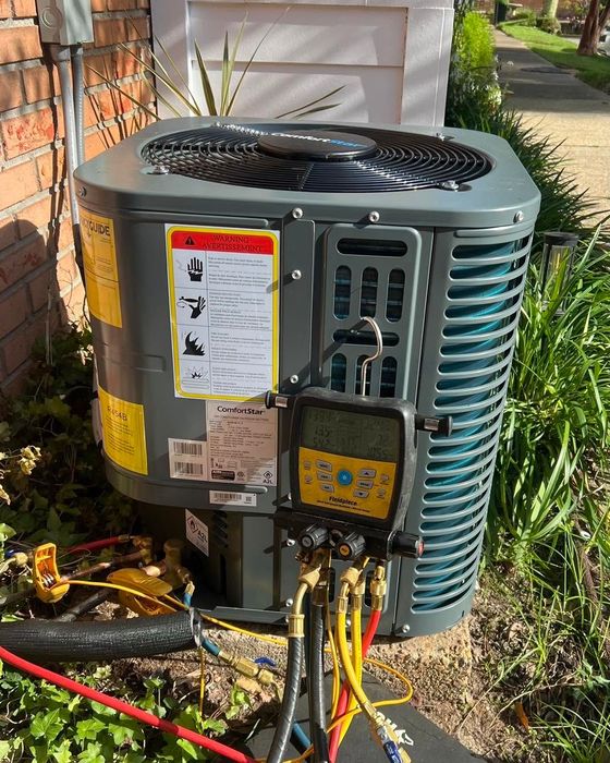 Outdoor central air conditioner unit with exposed service panel and connected hoses beside a house