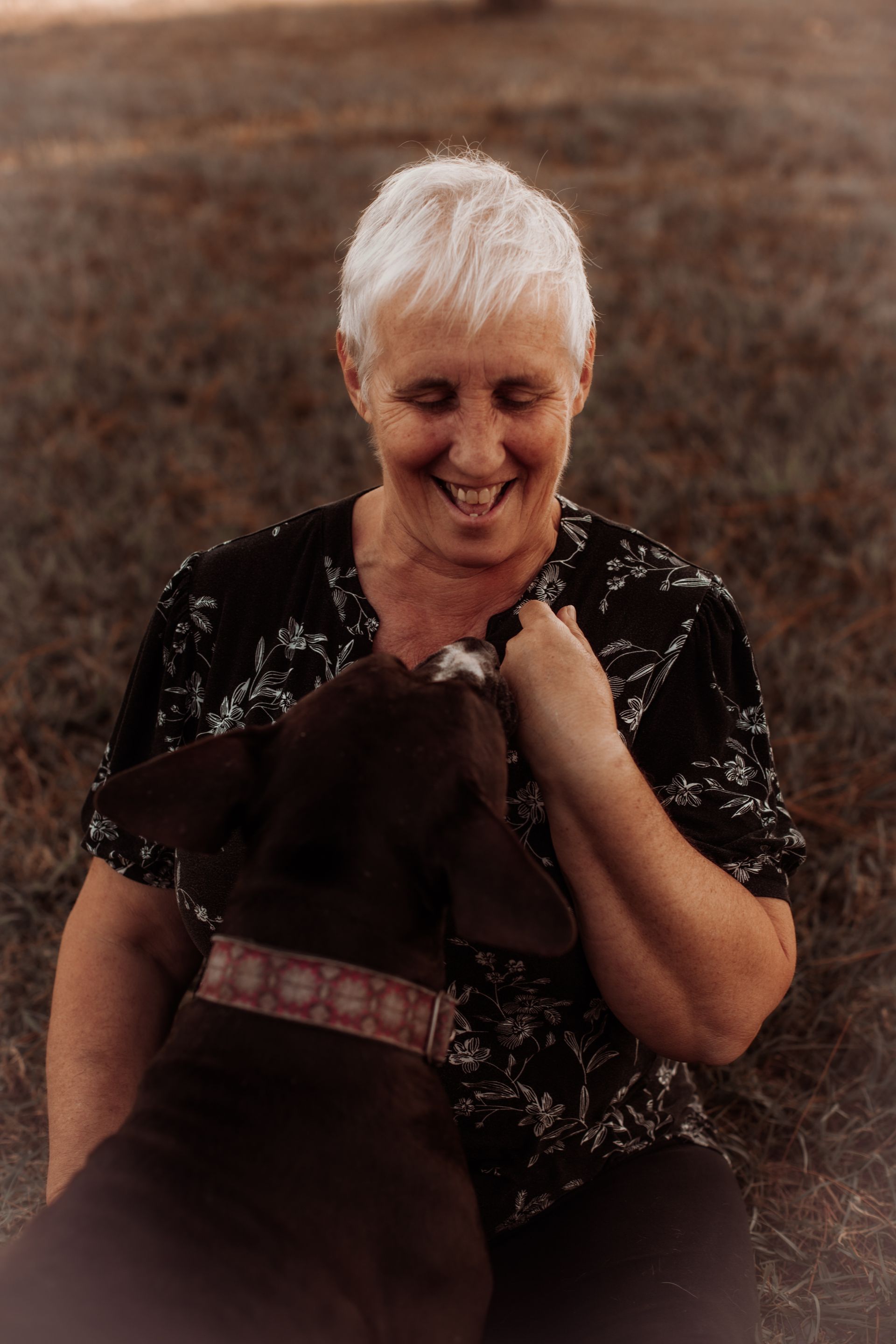 a woman is petting a brown dog in a field .