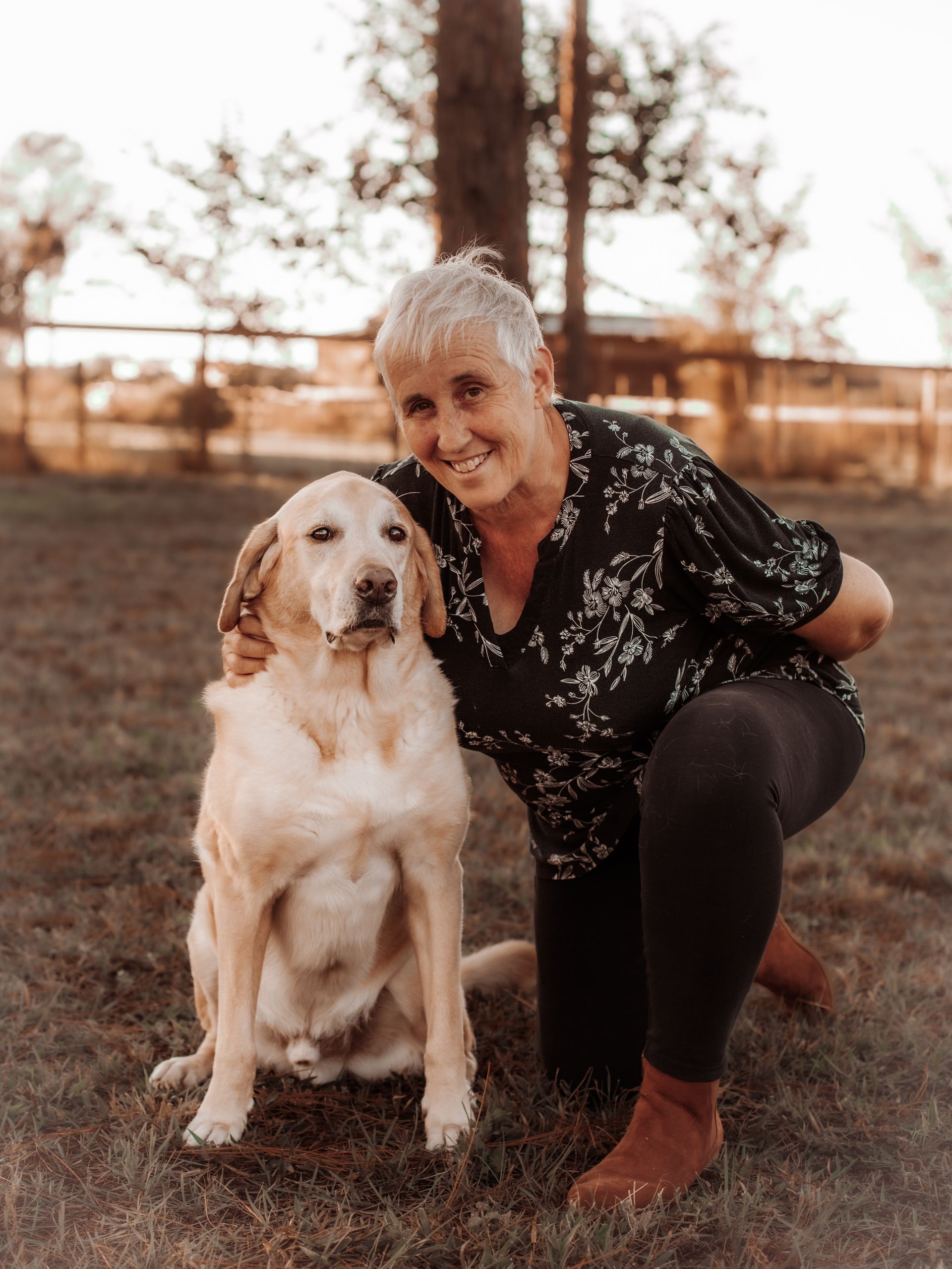 a woman is kneeling down next to a dog in the grass .