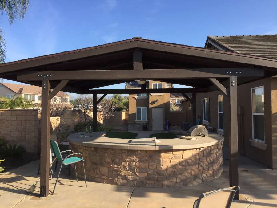 A patio with a wooden gazebo and a fire pit in the backyard of a house.