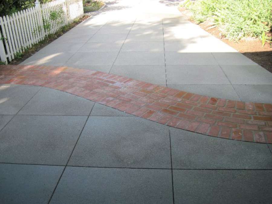 A driveway with a brick walkway and a white picket fence