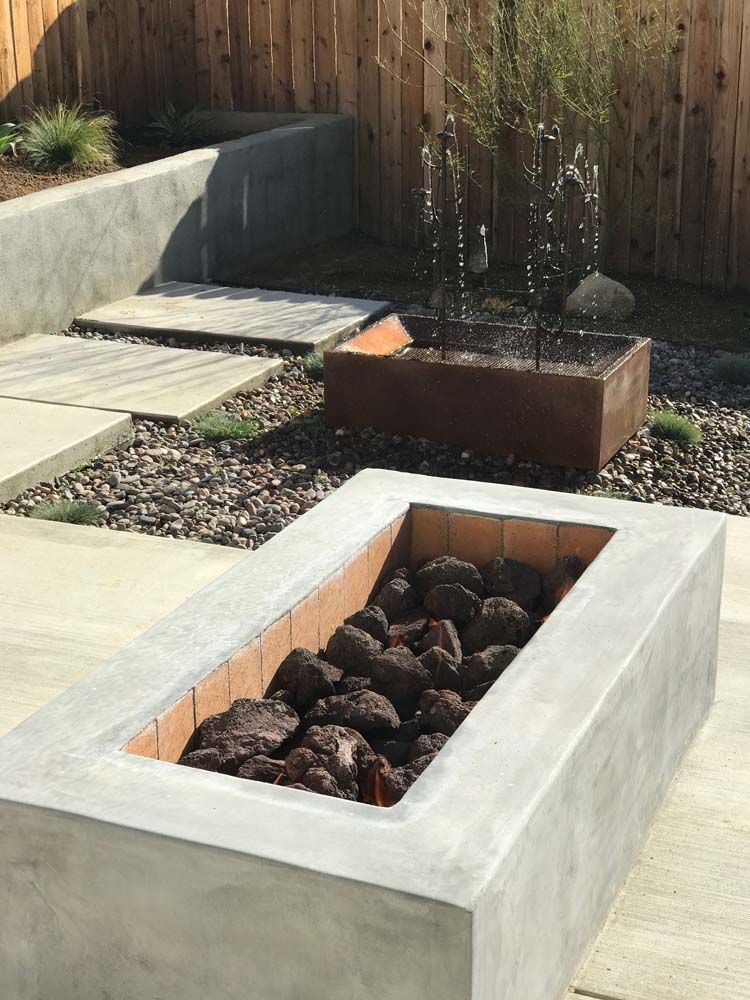 A concrete fire pit filled with rocks in a backyard.