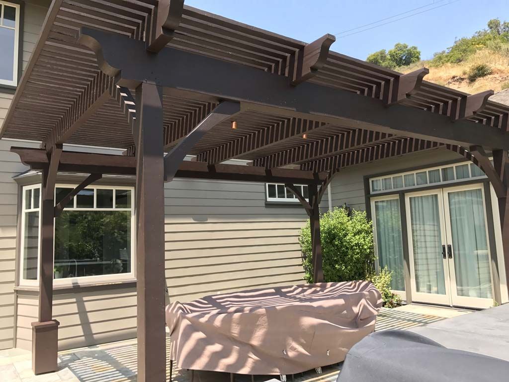 A wooden pergola is sitting on top of a patio next to a house.