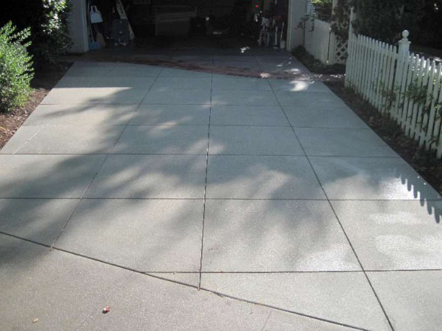 A concrete driveway with a white picket fence in the background