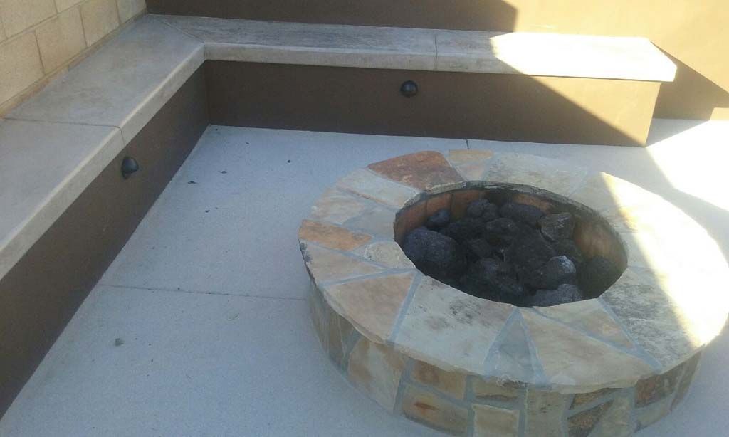 A fire pit is sitting on a concrete patio next to a bench.