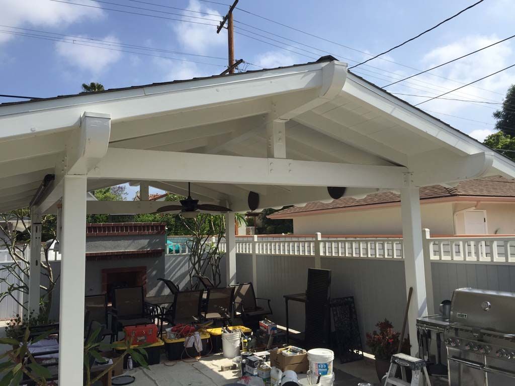 A white gazebo with a ceiling fan is being painted in a backyard.