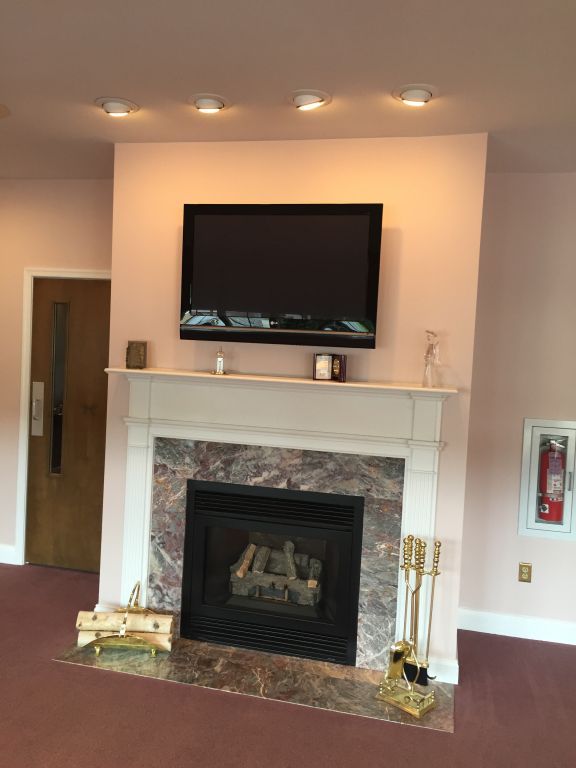 Fireplace with marble surround, a mounted TV, and fire tools, set in a pink-painted room. A wooden door and fire extinguisher are also visible.