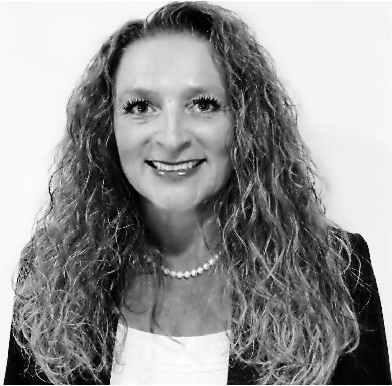 A woman with curly hair and a pearl necklace is smiling in a black and white photo.