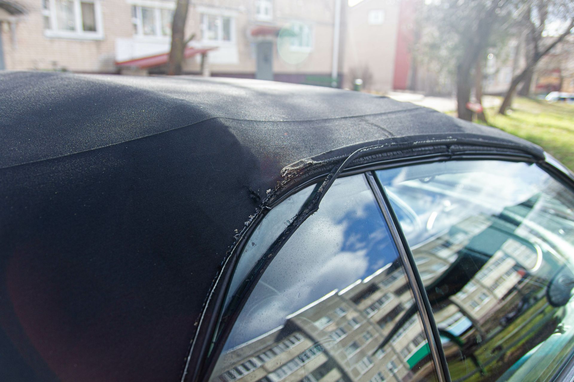 A black car with a convertible top is parked in front of a building.