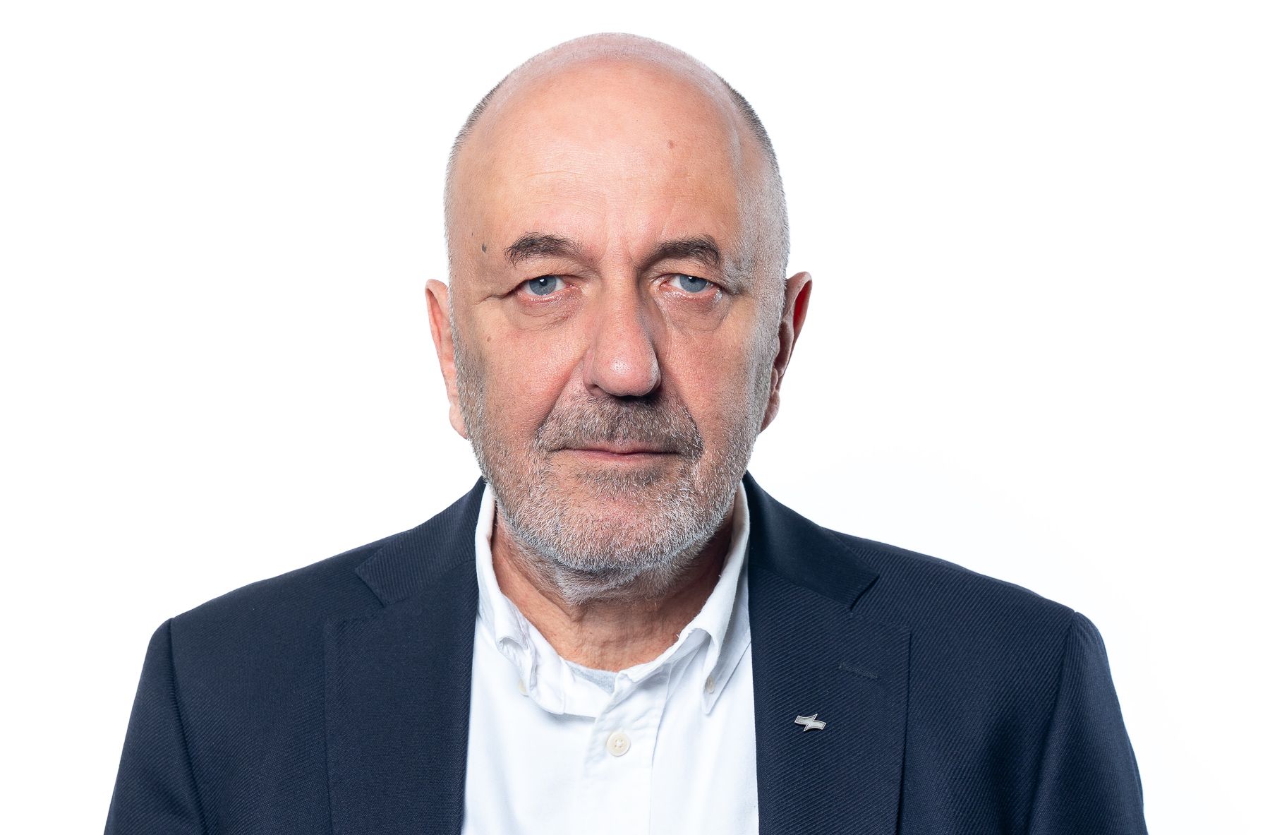 Porträt eines kahlköpfigen Mannes in einem dunklen Blazer und weißem Hemd vor weißem Hintergrund