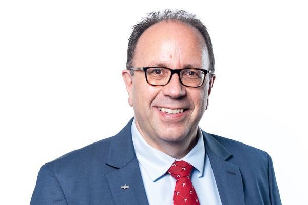 Lächelnder Mann in blauem Anzug, weißem Hemd und roter Krawatte vor weißem Hintergrund