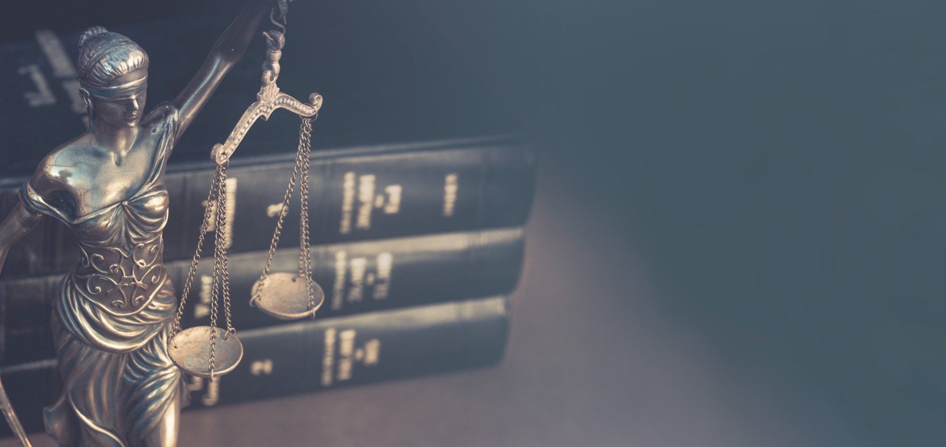 Justitia-Figur neben gestapelten Gesetzbüchern vor dunklem Hintergrund
