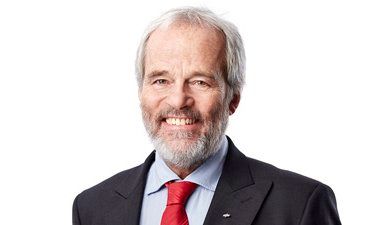 Lächelnder Mann in einem dunklen Anzug mit roter Krawatte vor weißem Hintergrund