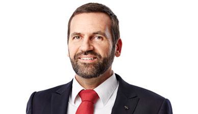 Lächelnder Mann in einem dunklen Anzug mit roter Krawatte vor weißem Hintergrund