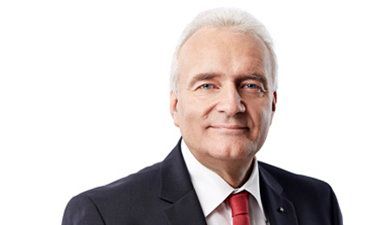 Porträt eines lächelnden Mannes in einem dunklen Anzug und roter Krawatte vor weißem Hintergrund