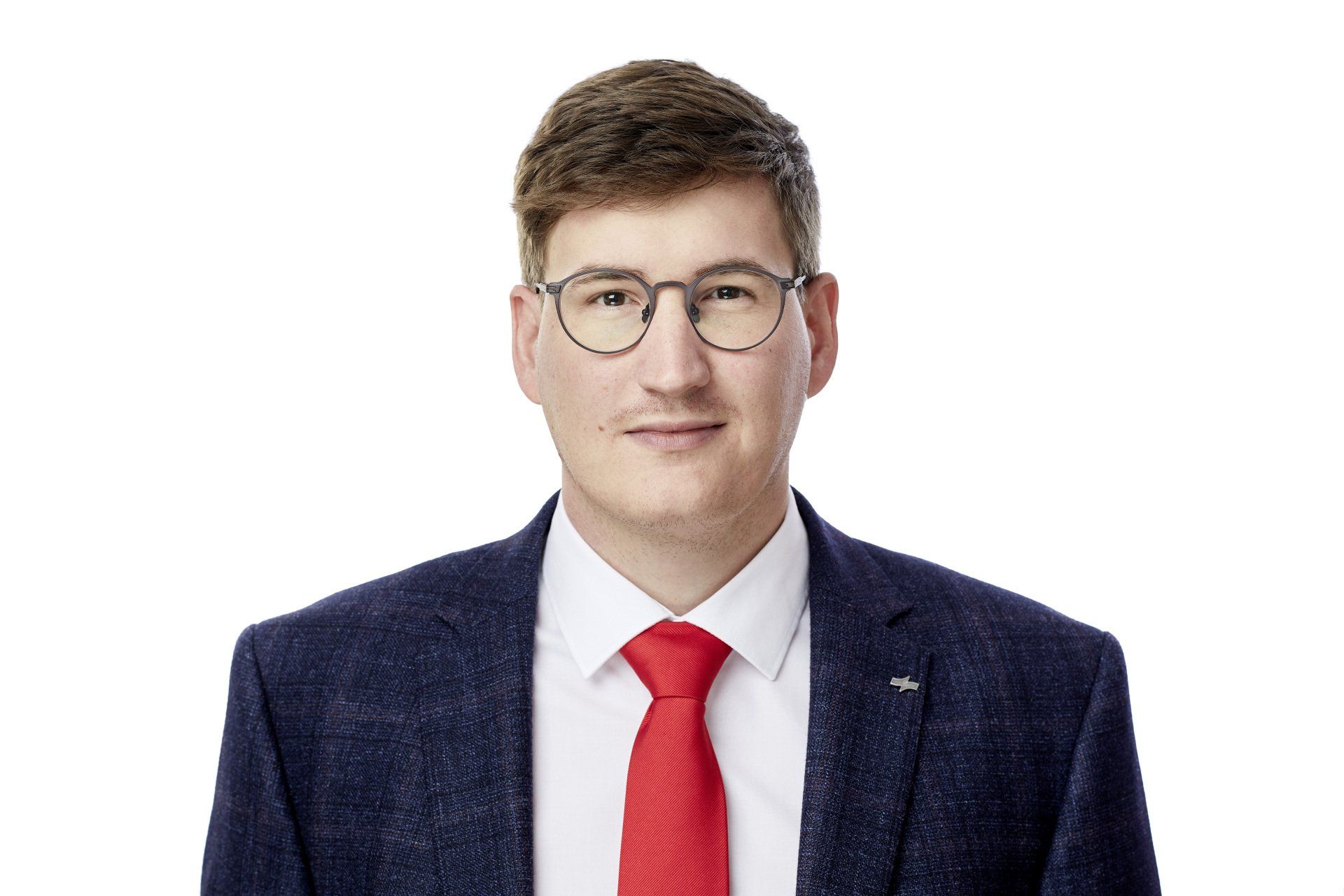Studioaufnahme eines Mannes mit Brille, dunkelblauem Anzug, weißem Hemd und roter Krawatte vor weißem Hintergrund