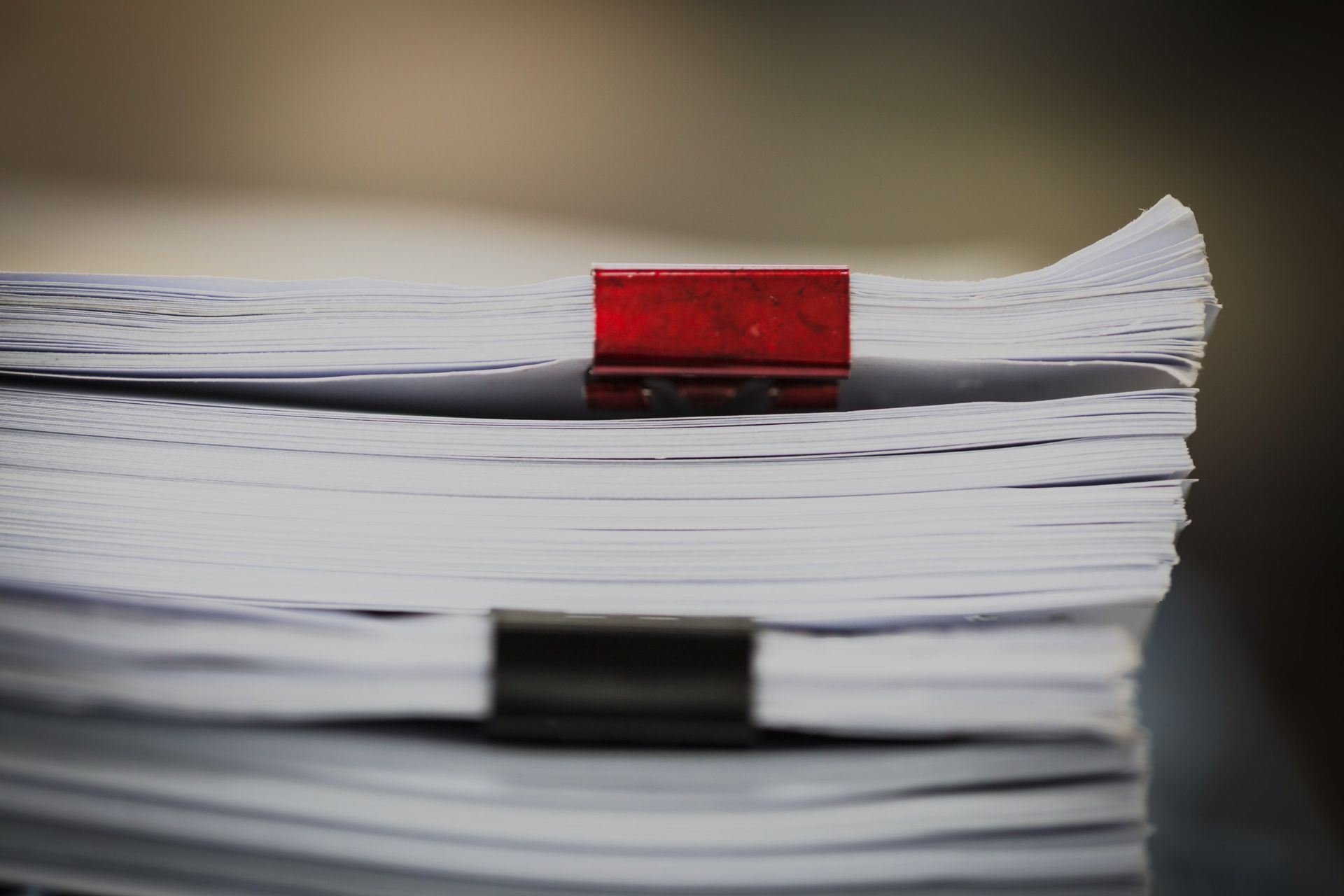 Ein Stapel Papier, zusammengehalten von einer roten Büroklammer oben und einer schwarzen Büroklammer unten.