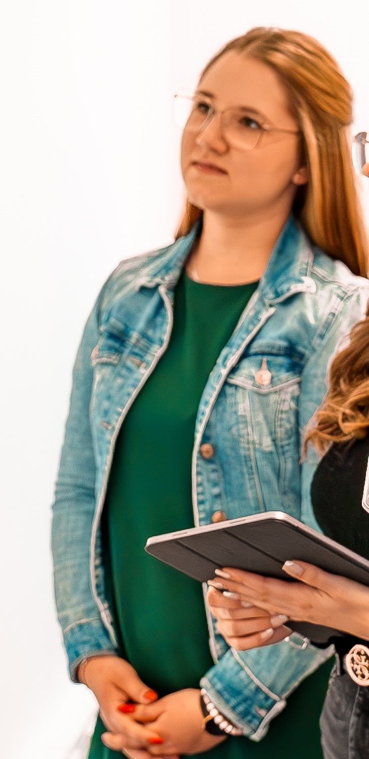 Eine Person in einer Jeansjacke hält ein Tablet und steht vor einem weißen Hintergrund.
