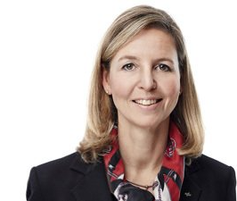 Studioaufnahme einer lächelnden Frau in einem schwarzen Blazer und einem rot gemusterten Schal vor weißem Hintergrund