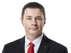 Porträt eines Mannes in schwarzem Anzug, weißem Hemd und roter Krawatte vor hellem Hintergrund