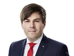 Porträt eines Mannes in einem dunkelblauen Anzug und roter Krawatte vor weißem Hintergrund