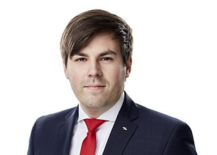 Formelles Porträt eines Mannes in dunklem Anzug, weißem Hemd und roter Krawatte vor weißem Hintergrund