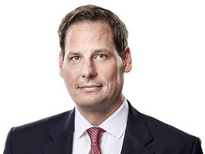 Porträt eines Mannes in einem dunklen Anzug und einer rot gestreiften Krawatte vor weißem Hintergrund