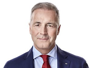 Studioaufnahme eines Mannes in einem dunkelblauen Anzug, hellblauem Hemd und roter Krawatte vor weißem Hintergrund