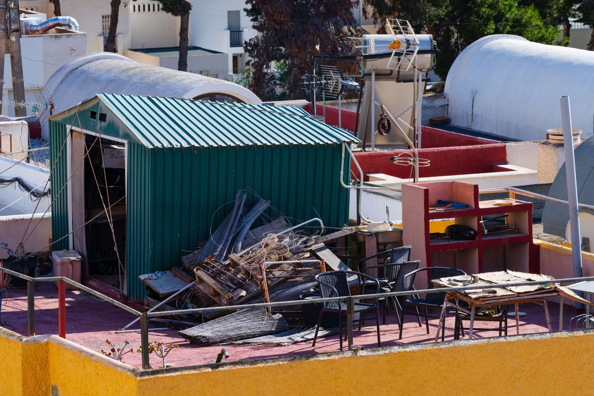 Construction debris in a green shed beside red machinery and large white tanks outdoors