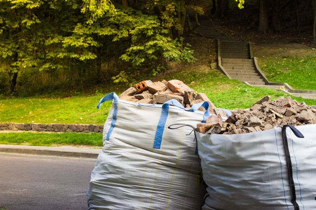 Two large white debris bags filled with rubble on a roadside near a grassy embankment and steps