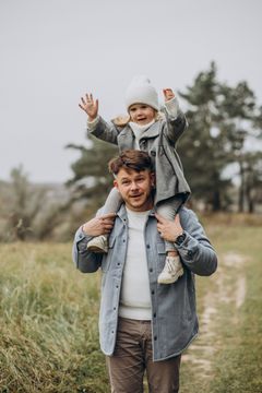 Father carrying a child on his shoulders, both smiling outside.
