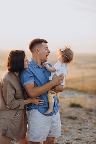 Family of three: father holding toddler, mother smiling, outdoors at sunset.