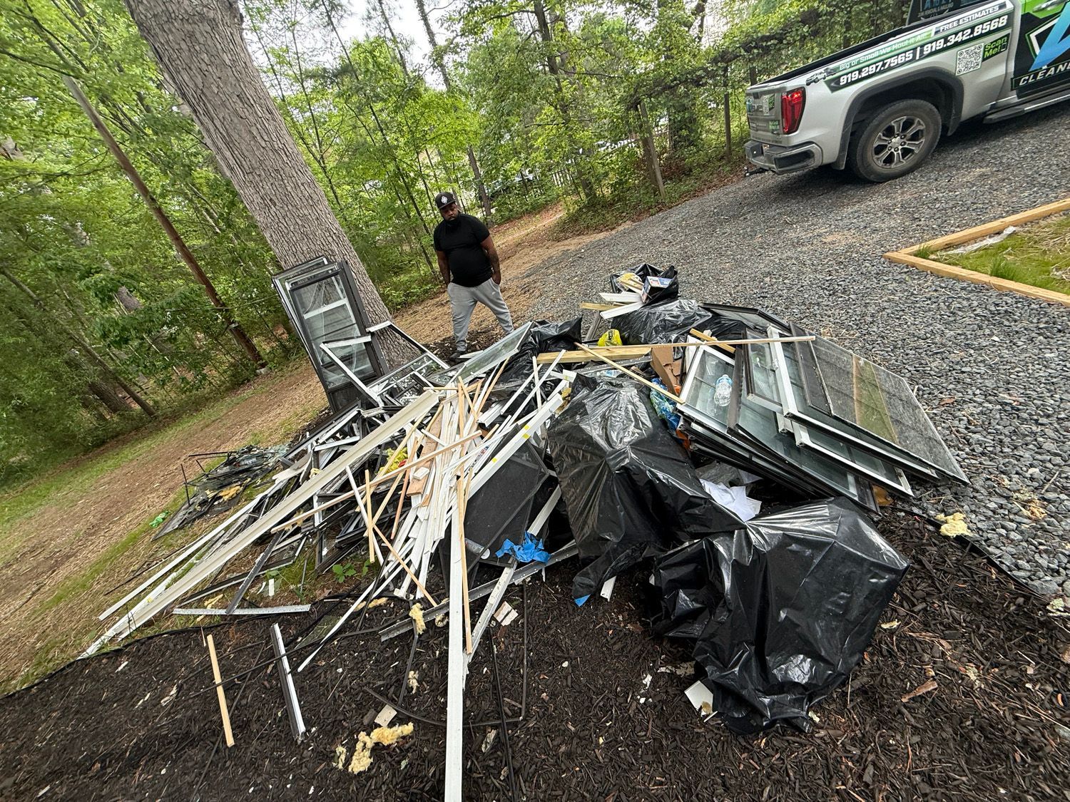 Pile of broken debris and metal on gravel driveway, with a person standing nearby and a truck parked beside it