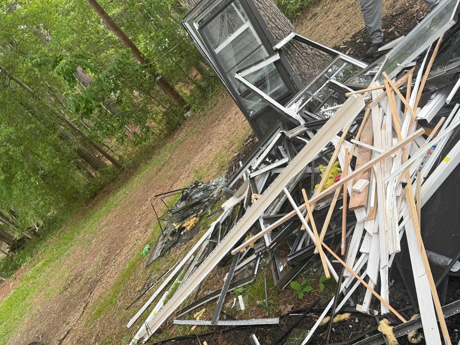Pile of broken white fence panels and wood debris in a wooded yard near a shed.