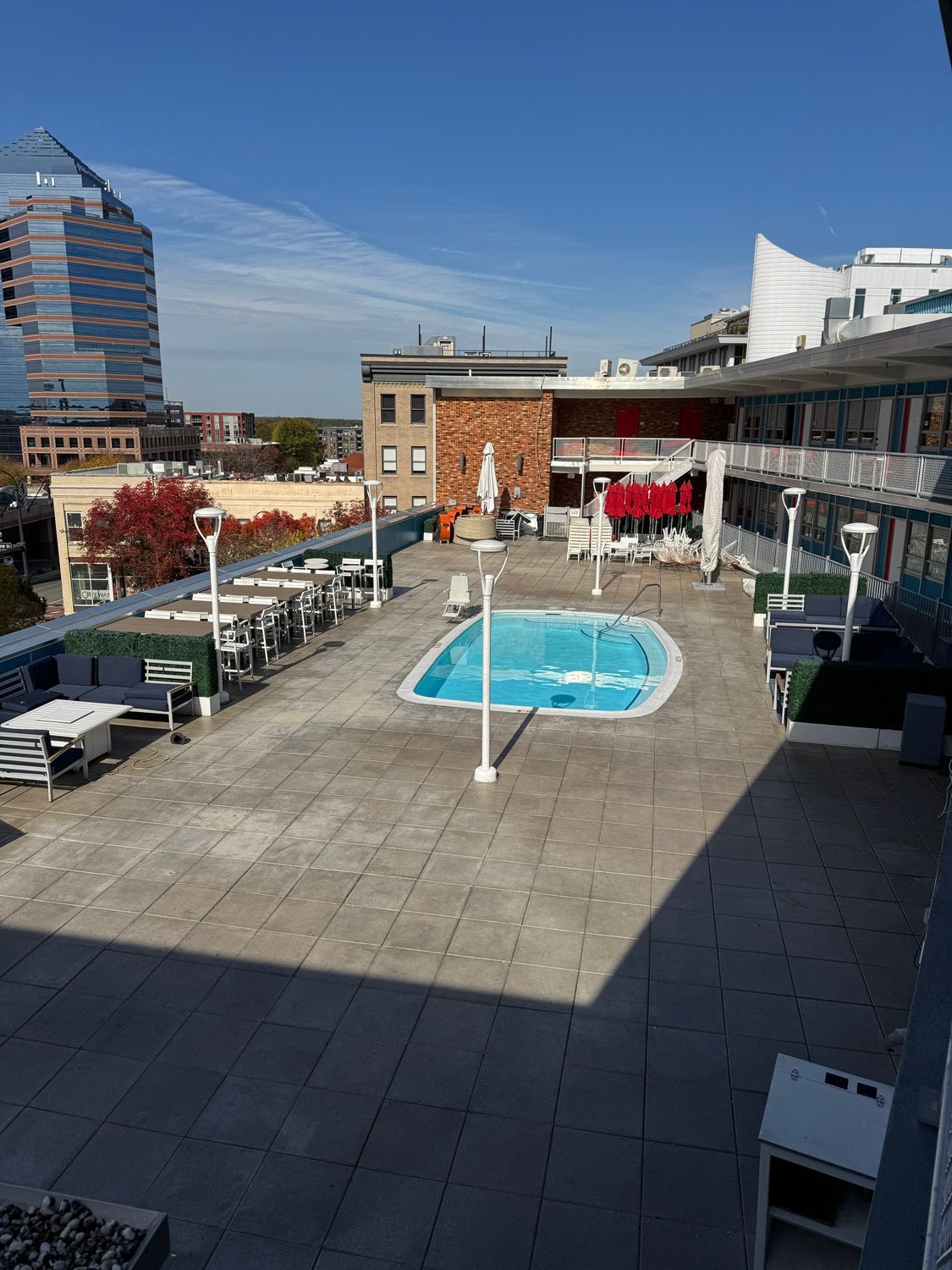 Rooftop terrace with a small blue pool, lounge seating, and city buildings under a clear sky
