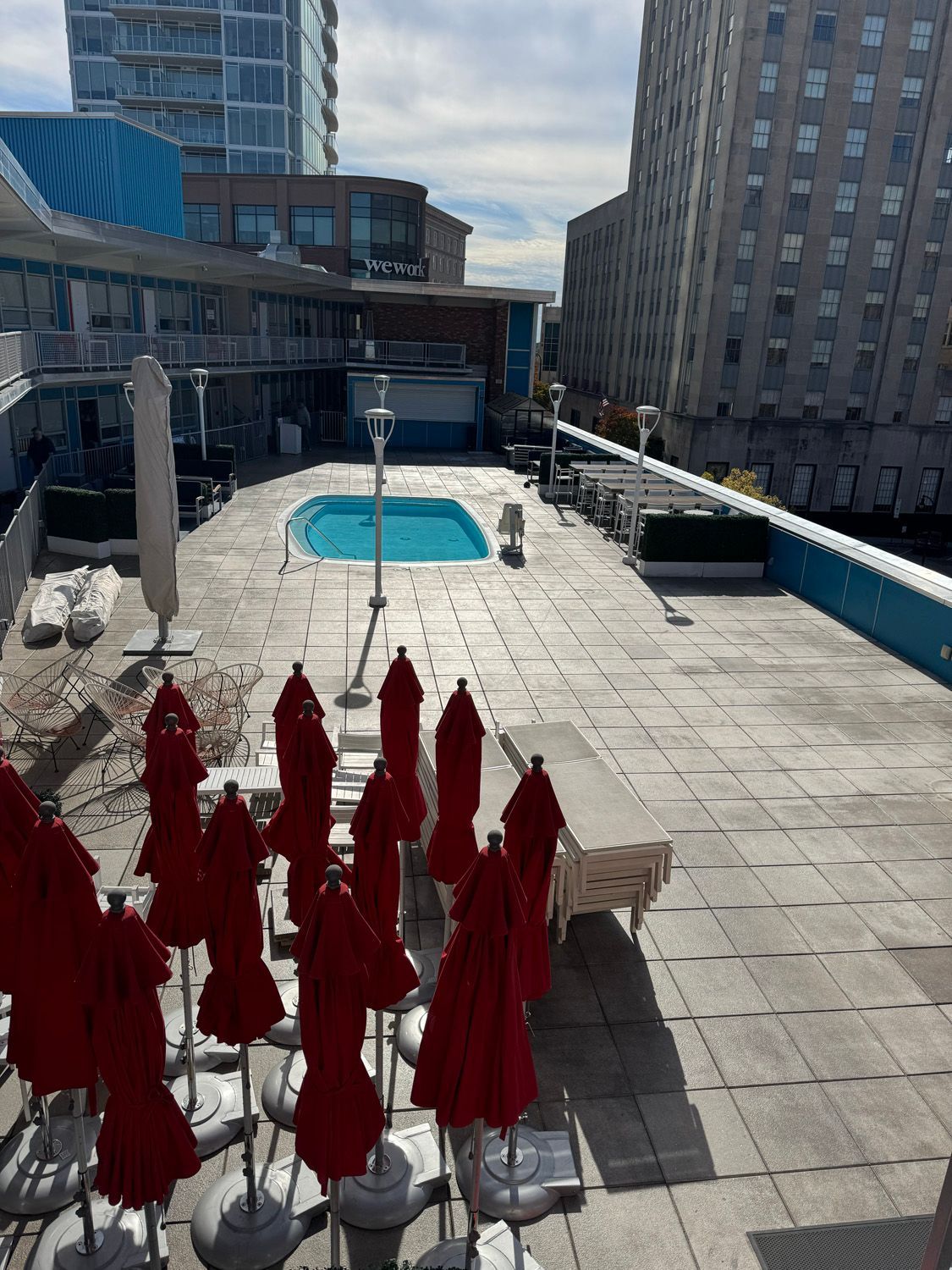 Rooftop patio with red umbrellas and a small blue pool between city buildings