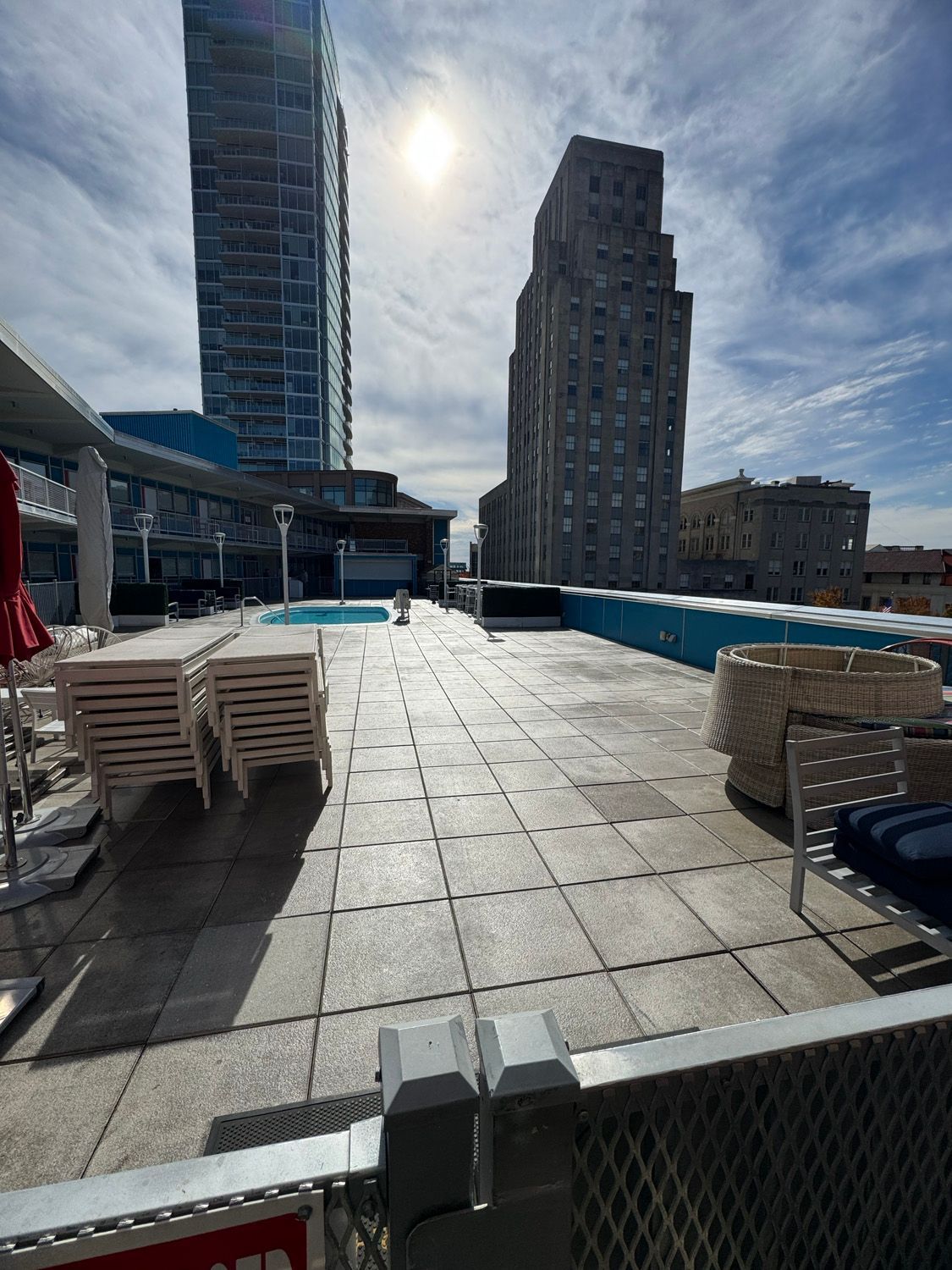 Rooftop pool deck with stacked lounge chairs, blue water, and tall buildings under a bright sun