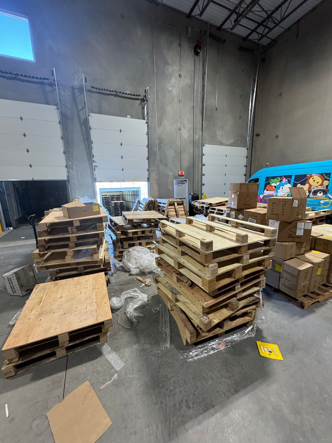 Warehouse floor with stacked wooden pallets, boxes, and plastic-wrapped materials near loading doors