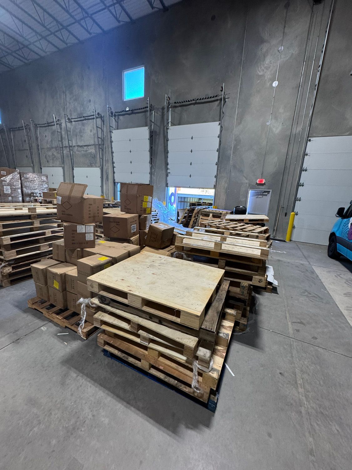 Warehouse with stacks of wooden pallets and boxes near large loading dock doors