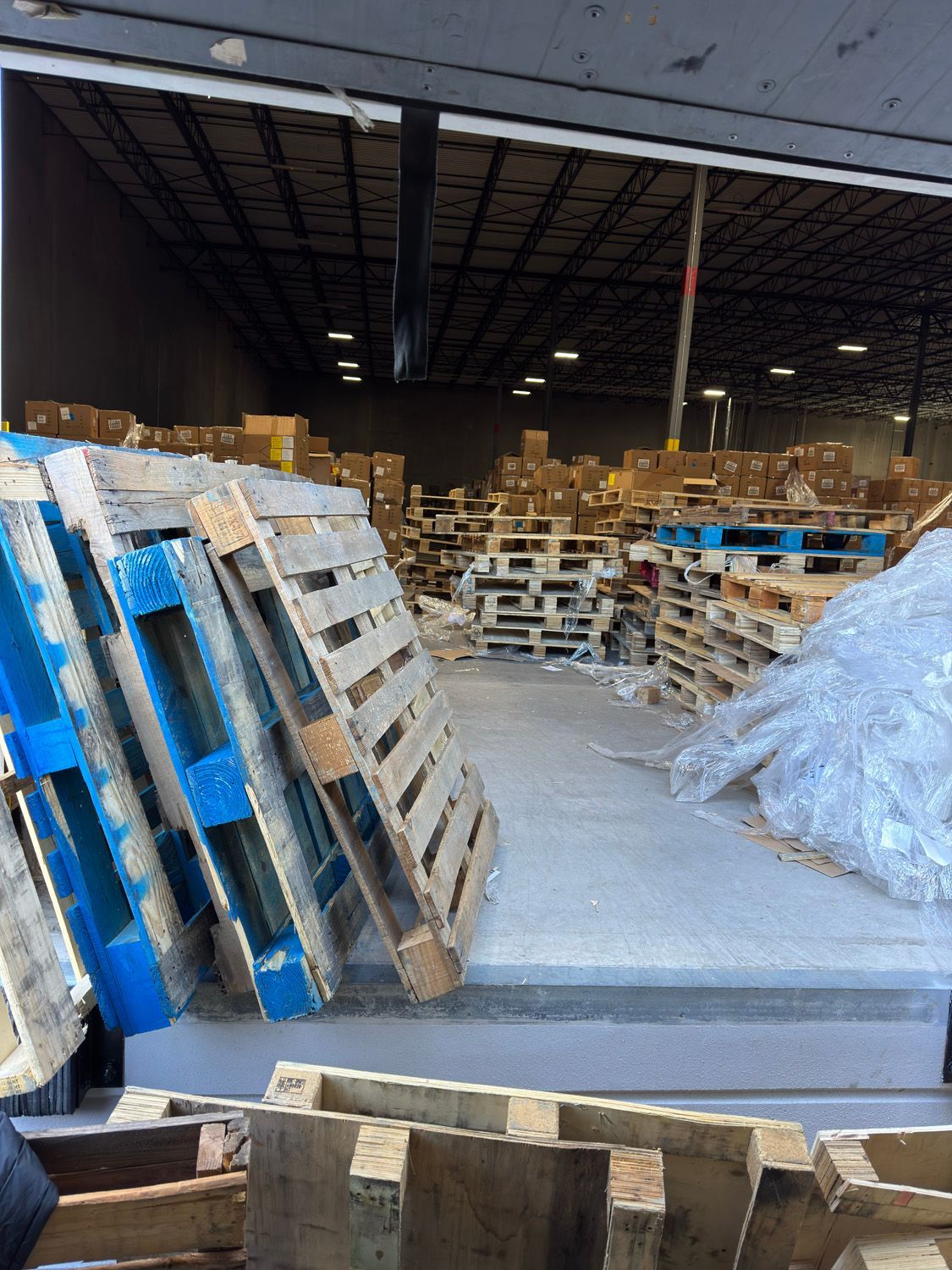 Warehouse aisle with stacked wooden pallets and shrink-wrapped goods under a dark ceiling