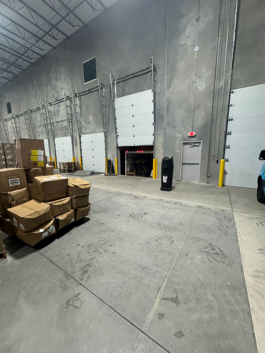 Warehouse loading dock with stacked cardboard boxes and closed roll-up doors on a concrete floor.