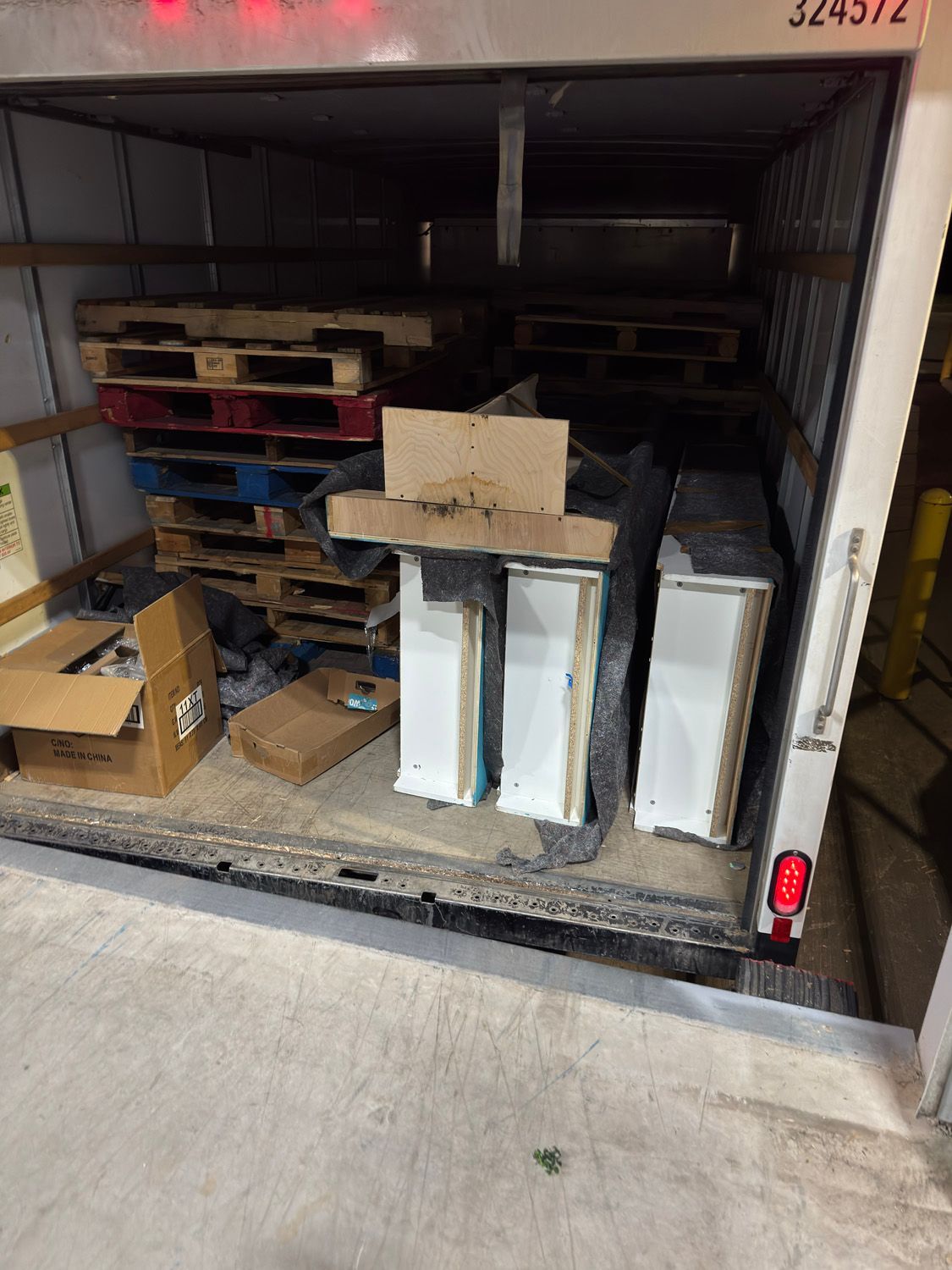 Trailer loaded with stacked wooden pallets and boxes, viewed from the open rear.