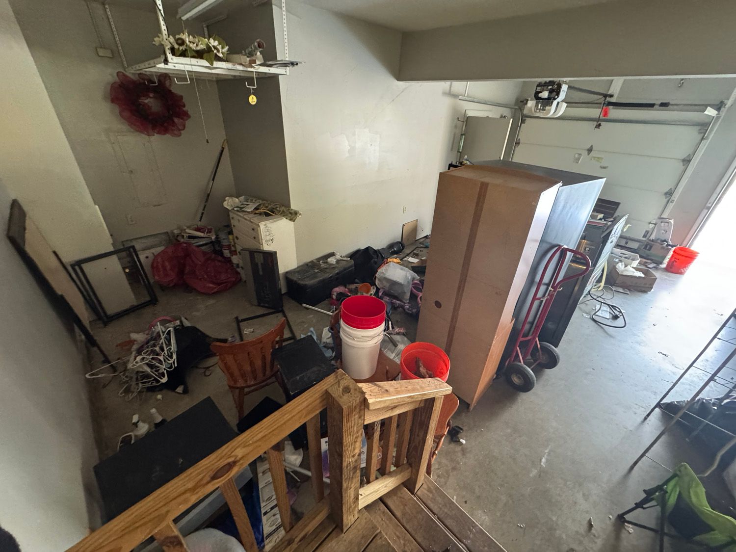 Cluttered garage with tools, storage bins, and a ladder near an open garage door.