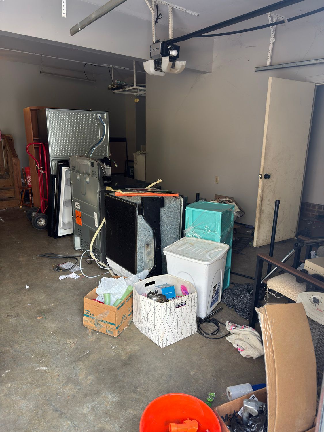 Cluttered garage with storage bins, boxes, and household items stacked along the wall.