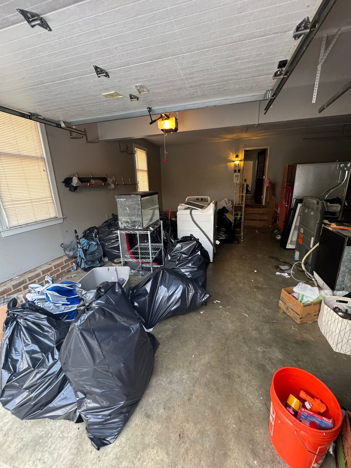 Cluttered garage with black trash bags, boxes, and stored items along both walls