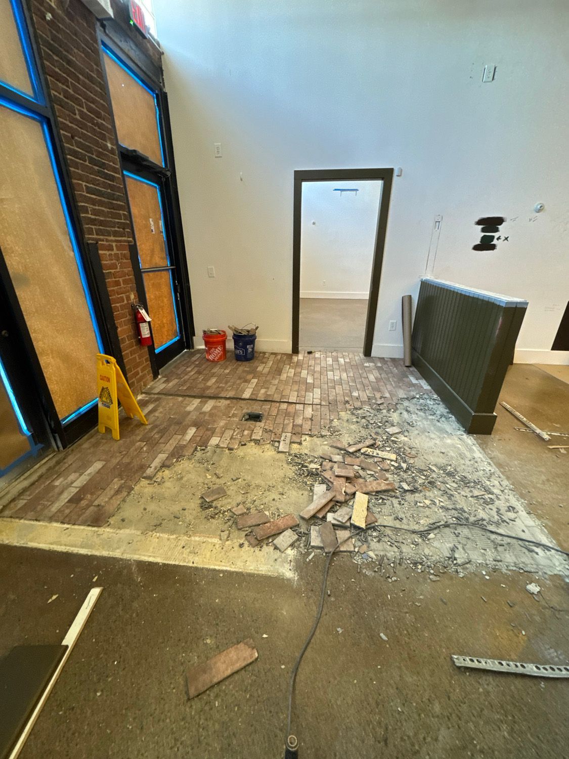 Damaged floor in a room with exposed wall framing, debris, and a doorway at the back.